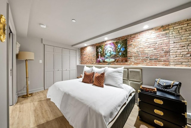 bedroom featuring brick wall, baseboards, recessed lighting, light wood-style flooring, and a closet