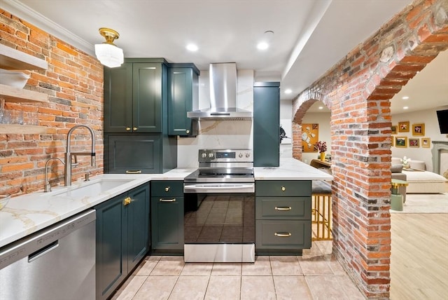 kitchen with green cabinetry, appliances with stainless steel finishes, a sink, and wall chimney range hood