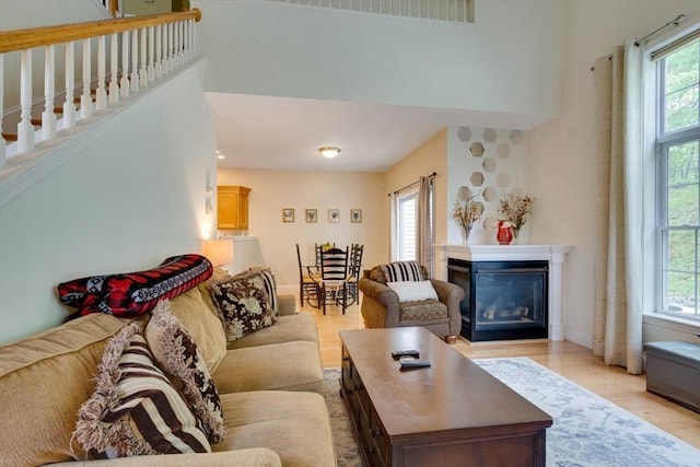 living area featuring a glass covered fireplace, a towering ceiling, light wood-style floors, and baseboards