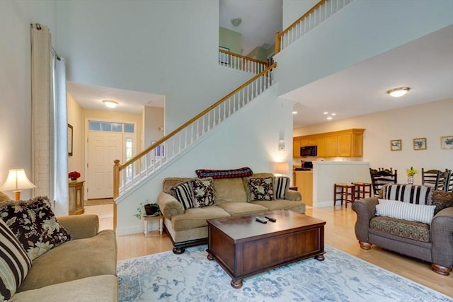 living area with a towering ceiling, stairway, and light wood-type flooring