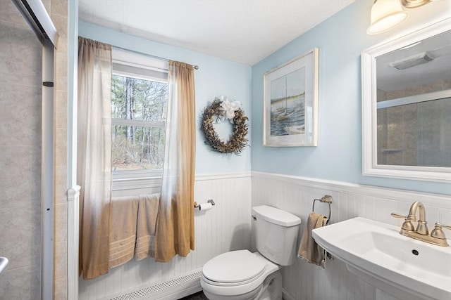 full bath featuring a shower stall, baseboard heating, a sink, wainscoting, and toilet