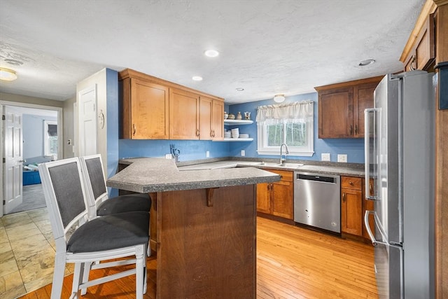 kitchen featuring light wood finished floors, stainless steel appliances, open shelves, a peninsula, and a breakfast bar area