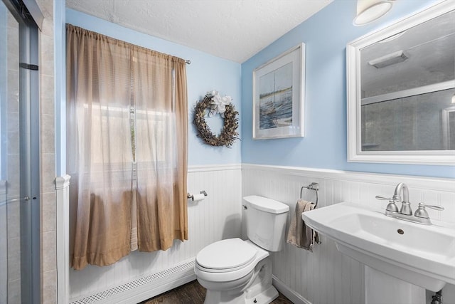 full bathroom with a tile shower, a wainscoted wall, toilet, a sink, and a baseboard radiator
