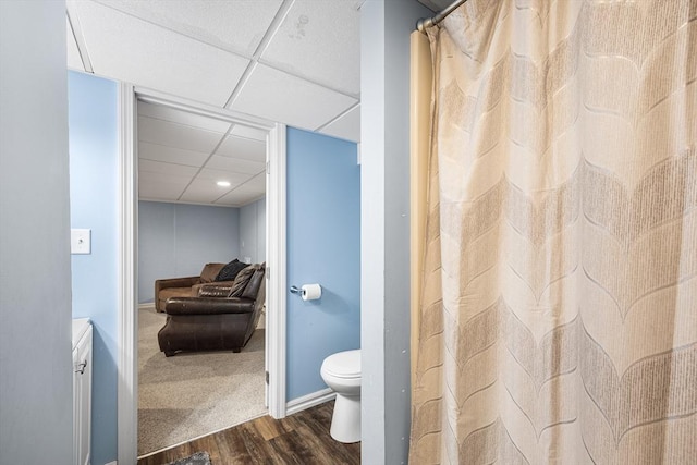 bathroom with curtained shower, wood finished floors, toilet, and a drop ceiling