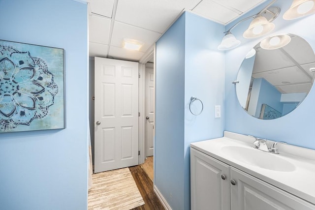 bathroom featuring baseboards, a paneled ceiling, wood finished floors, and vanity
