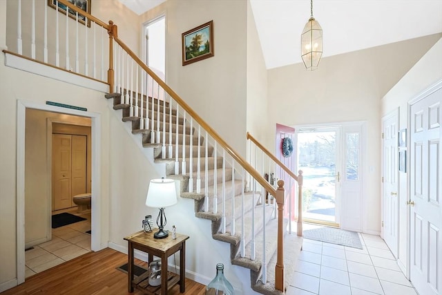 entryway featuring stairs, a towering ceiling, baseboards, and wood finished floors