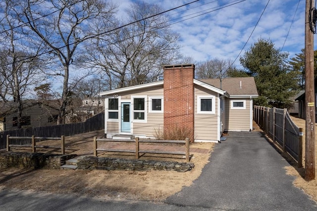 bungalow-style home featuring a fenced front yard, a chimney, and aphalt driveway