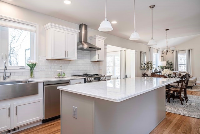 kitchen featuring wall chimney range hood, light hardwood / wood-style floors, and decorative light fixtures