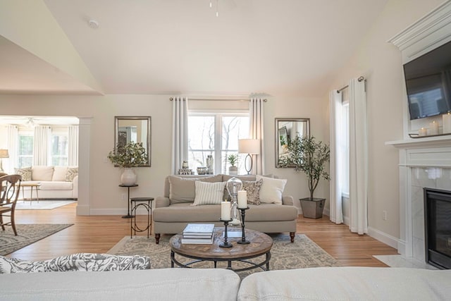 living room with a tiled fireplace, lofted ceiling, a wealth of natural light, and light hardwood / wood-style flooring