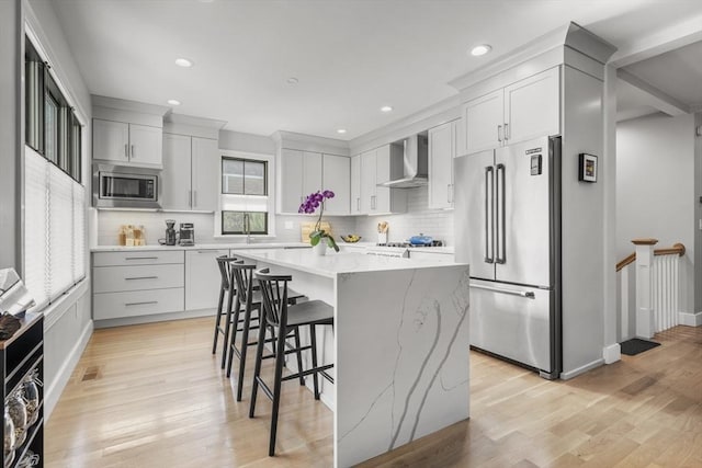 kitchen with a center island, a kitchen breakfast bar, backsplash, wall chimney range hood, and appliances with stainless steel finishes