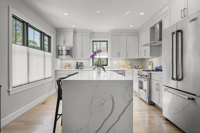 kitchen with a kitchen island, high end appliances, a healthy amount of sunlight, and wall chimney exhaust hood