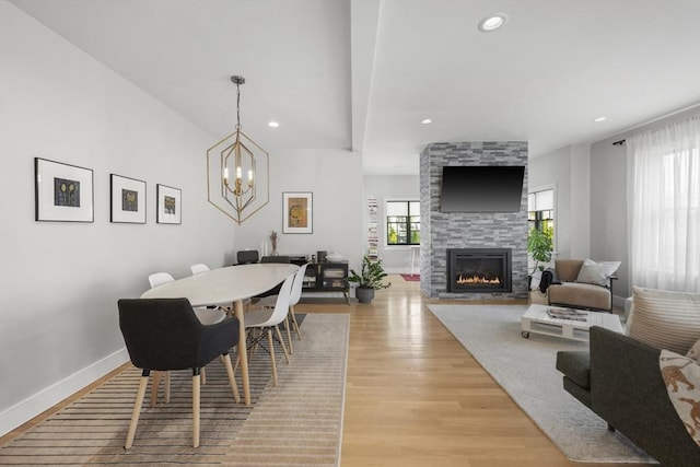 dining space featuring baseboards, a large fireplace, light wood-style floors, a chandelier, and recessed lighting