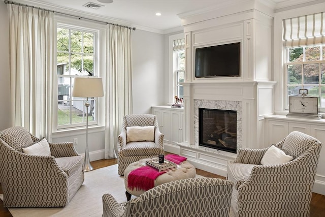 living area with crown molding, recessed lighting, visible vents, light wood-style flooring, and a premium fireplace