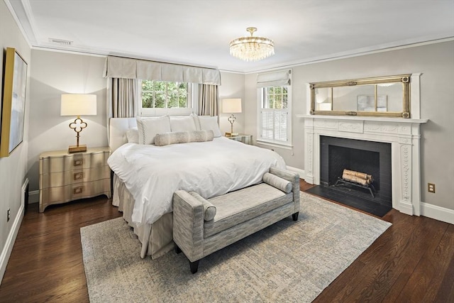 bedroom featuring baseboards, a fireplace with flush hearth, wood finished floors, crown molding, and a chandelier