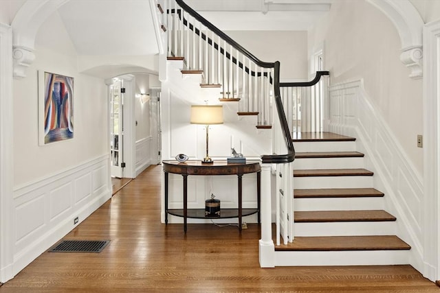 stairs with arched walkways, a decorative wall, wood finished floors, visible vents, and wainscoting