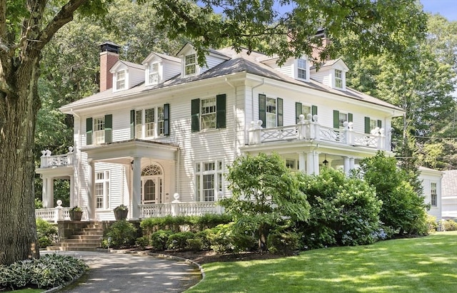 view of front of house with a front lawn, covered porch, a chimney, and a balcony