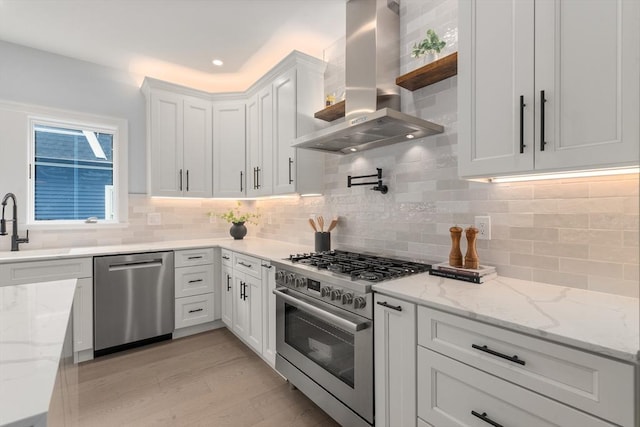 67 Pine St Unit 2, Dedham, MA 02026 - kitchen featuring island exhaust hood, stainless steel appliances, white cabinets, light wood-style floors, and decorative backsplash