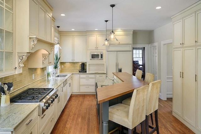 kitchen with built in appliances, a kitchen breakfast bar, wood finished floors, and a sink