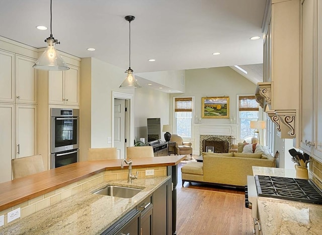 kitchen with stainless steel double oven, light wood-style flooring, a fireplace, a sink, and decorative light fixtures