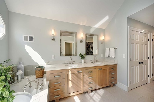 bathroom with double vanity, visible vents, vaulted ceiling, and a sink