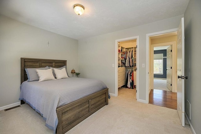 bedroom with visible vents, light carpet, a closet, baseboards, and a spacious closet