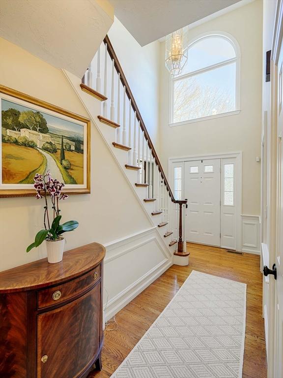 entryway featuring stairway, wood finished floors, a towering ceiling, wainscoting, and a decorative wall