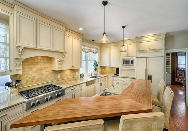 kitchen featuring decorative backsplash, decorative light fixtures, built in appliances, and a sink