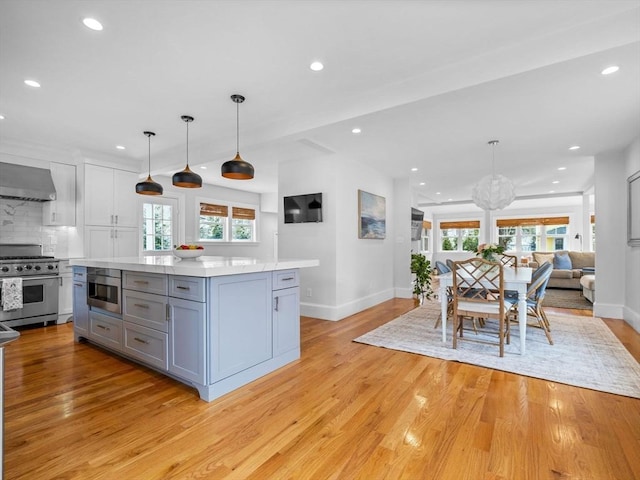 kitchen with gray cabinets, light countertops, high end stainless steel range oven, light wood-style flooring, and decorative backsplash