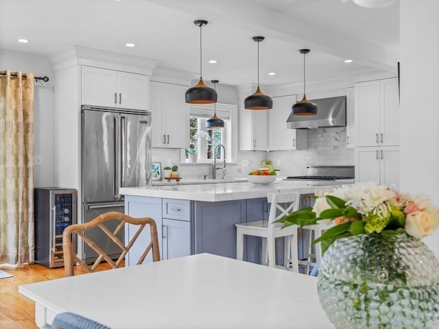 kitchen with high quality fridge, a sink, white cabinets, light countertops, and wall chimney range hood