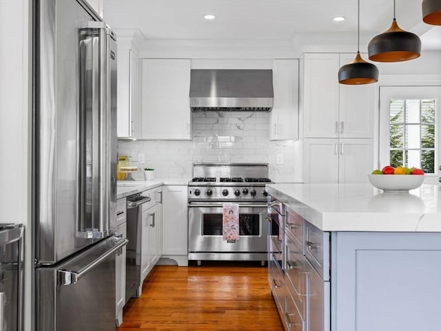 kitchen with appliances with stainless steel finishes, white cabinetry, wall chimney exhaust hood, and light stone countertops