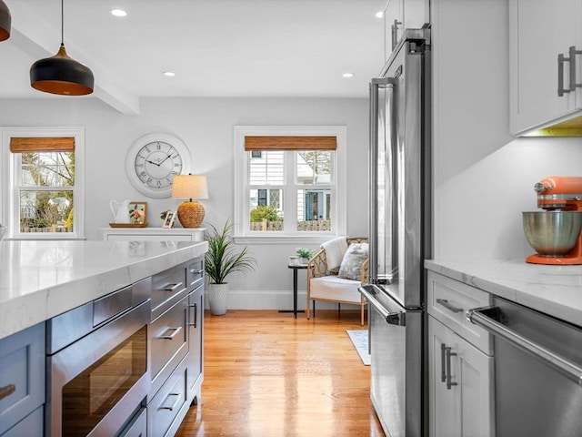 kitchen featuring a healthy amount of sunlight, light wood-style floors, appliances with stainless steel finishes, and light stone countertops