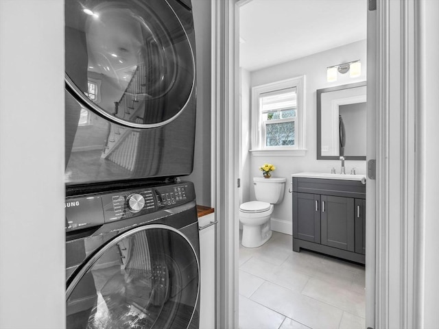 bathroom featuring baseboards, stacked washer and clothes dryer, toilet, tile patterned flooring, and vanity