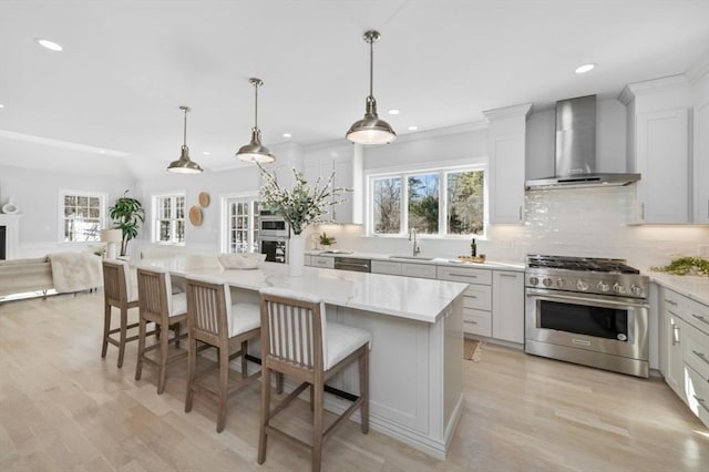 kitchen with appliances with stainless steel finishes, a center island, wall chimney range hood, and decorative light fixtures