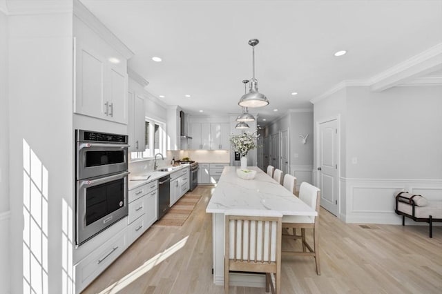 kitchen featuring light hardwood / wood-style flooring, appliances with stainless steel finishes, a kitchen island, pendant lighting, and white cabinets