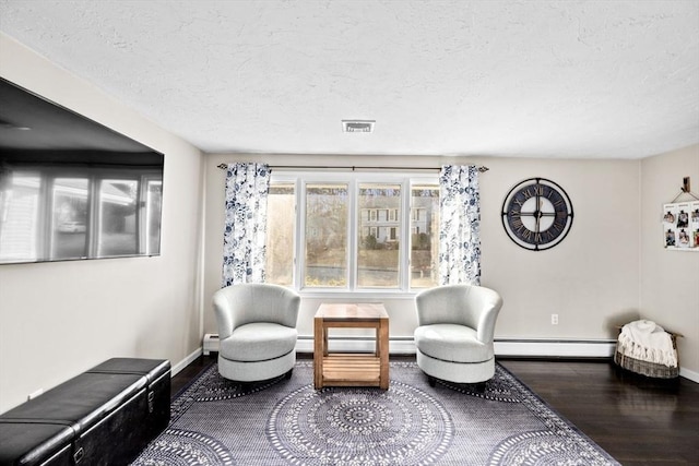 living area featuring visible vents, a textured ceiling, wood finished floors, a baseboard radiator, and baseboards