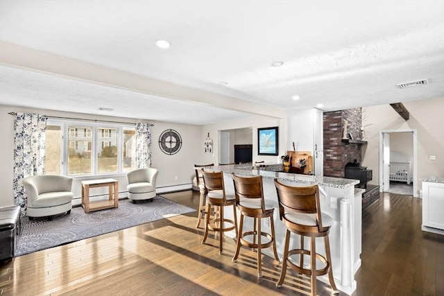 kitchen with light stone countertops, visible vents, dark wood-style flooring, a baseboard heating unit, and open floor plan