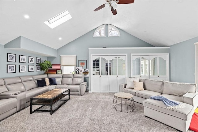 carpeted living room with vaulted ceiling with skylight and a ceiling fan