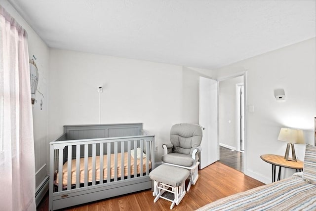 bedroom with a nursery area, wood finished floors, and baseboards