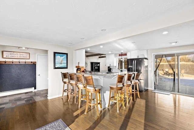 kitchen featuring a breakfast bar, white cabinets, wood-type flooring, fridge with ice dispenser, and baseboard heating