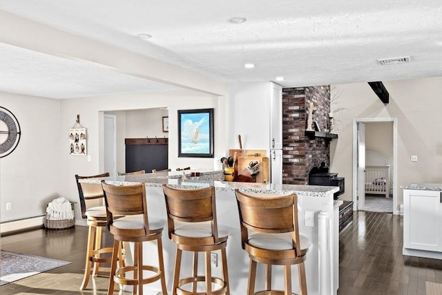 bar with visible vents, baseboard heating, a textured ceiling, and dark wood-style flooring