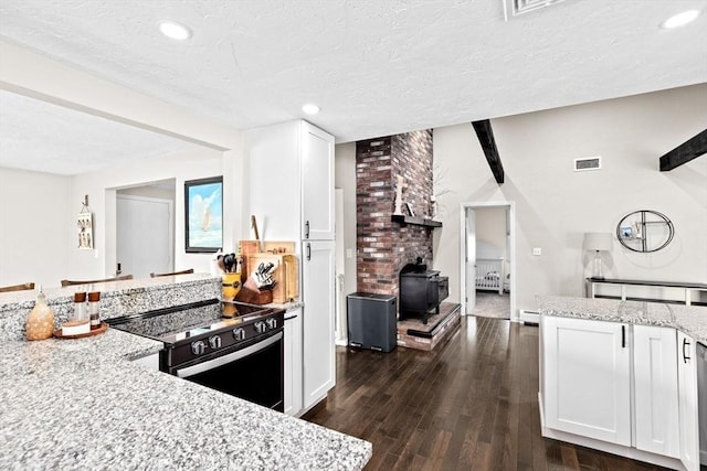 kitchen with visible vents, black range with electric cooktop, a wood stove, dark wood-style floors, and white cabinetry