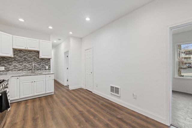 kitchen with light stone countertops, dark hardwood / wood-style floors, white cabinetry, and sink