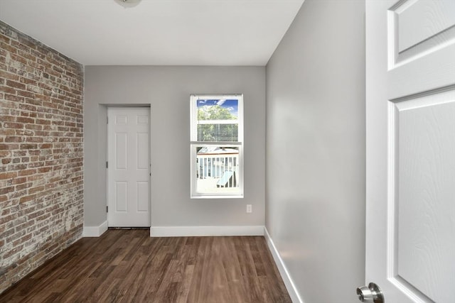 unfurnished room featuring dark hardwood / wood-style floors and brick wall