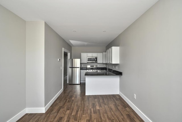 kitchen with kitchen peninsula, white cabinets, stainless steel appliances, and dark hardwood / wood-style floors