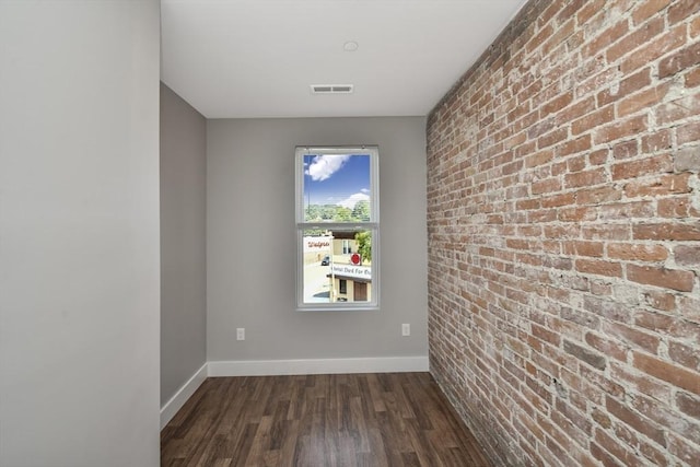 empty room featuring dark wood-type flooring and brick wall