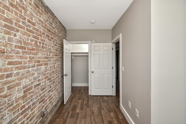 hallway with dark hardwood / wood-style flooring and brick wall