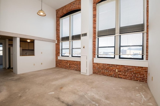 unfurnished living room featuring light carpet, brick wall, and a high ceiling