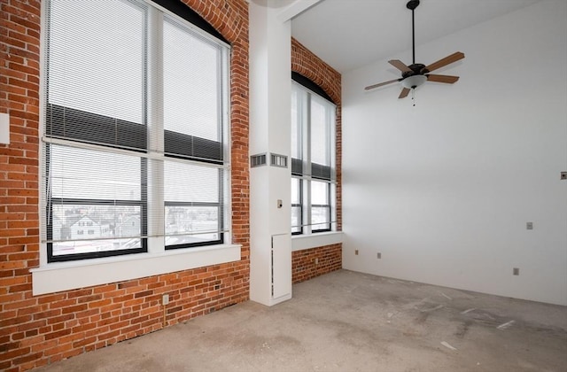 spare room with a high ceiling, brick wall, and ceiling fan