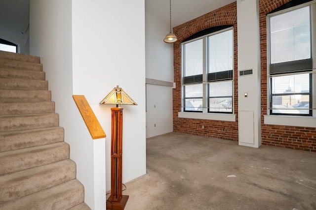 interior space with a high ceiling, brick wall, plenty of natural light, and carpet floors