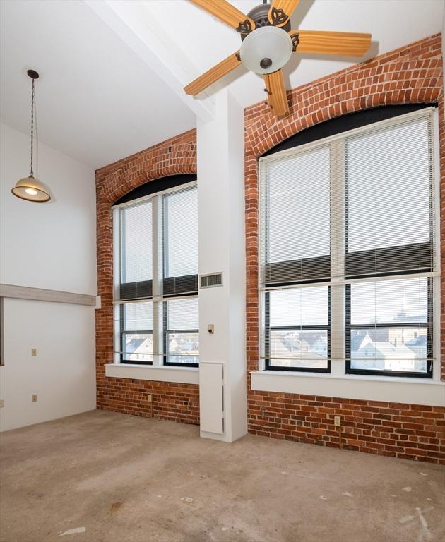 unfurnished living room with a wealth of natural light, high vaulted ceiling, and brick wall